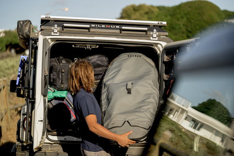 ION Wing Boardbag Core in dark grey being loaded into a vehicle at a watersports location