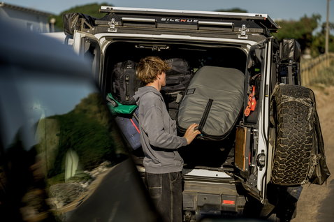 ION Wing Boardbag Core Slim em verde-oliva escuro a ser carregado num veículo todo-o-terreno