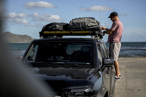 ION Wing Gearbag Core travel bag in charcoal being loaded onto a roof rack at the coast