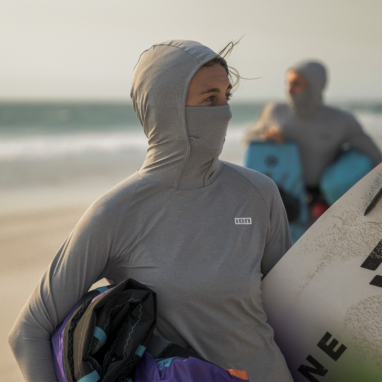 Top ION Storm Pro LS UV lycra con cappuccio da donna durante il kitesurf in spiaggia in grigio chiaro