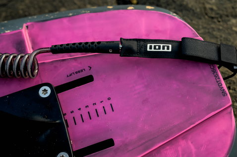 ION Core leash ginocchio arrotolata in nero, dettaglio su foil board rosa