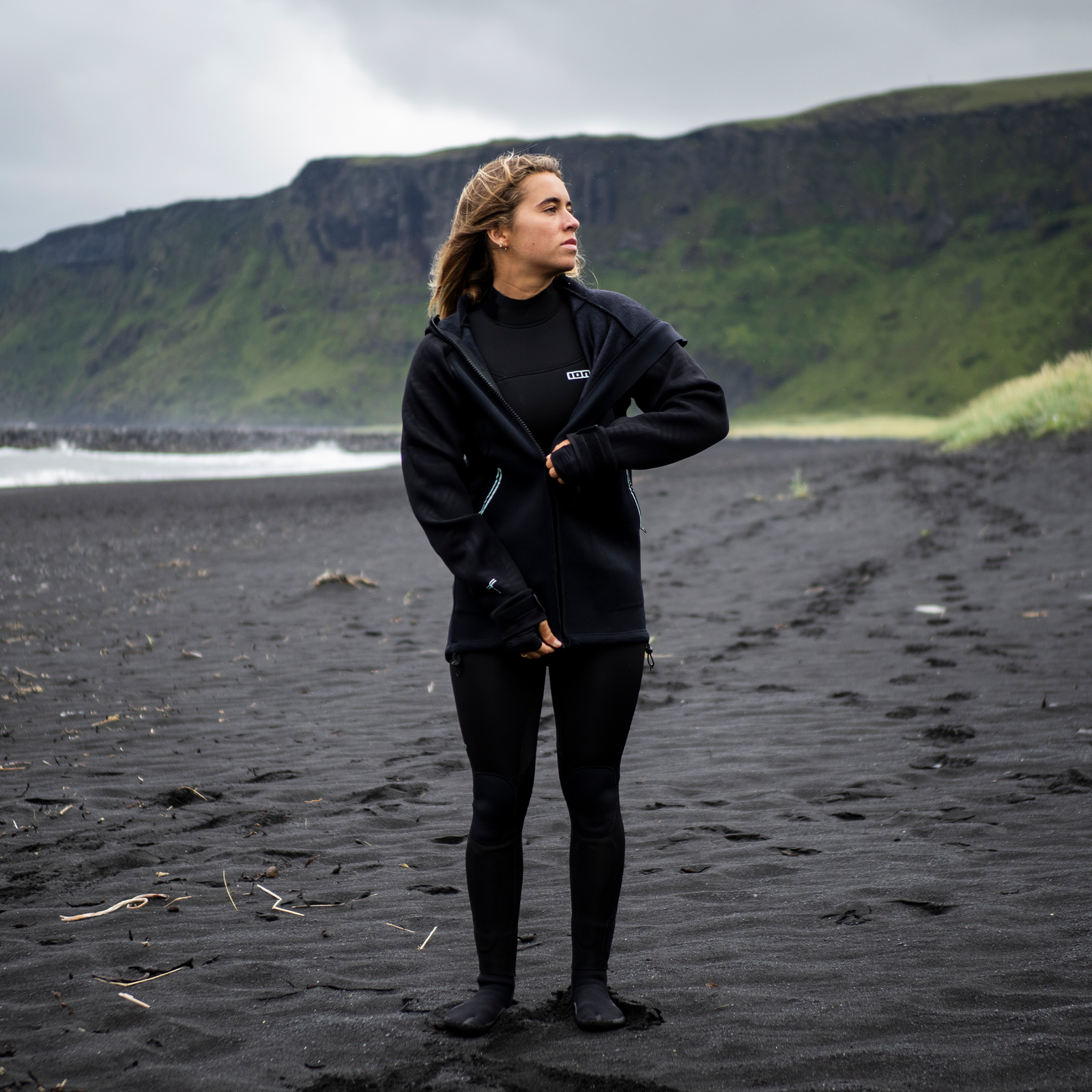 ION Neo Shelter Jacket Amp Damen Neoprenjacke in schwarz beim Tragen an einem schwarzen Sandstrand