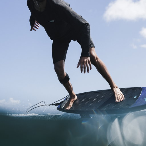 Surfer on Duotone pronefoil riding a wave, wearing ION Surf Shield cut‑resistant tights.