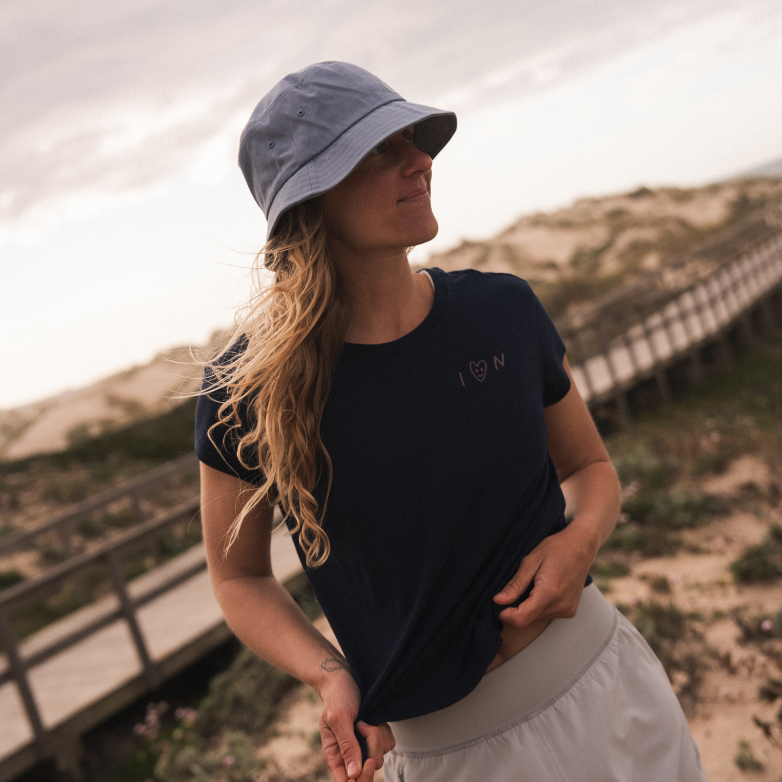 ION Bucket Hat in light blue worn by a woman at the beach with sand dunes in the background