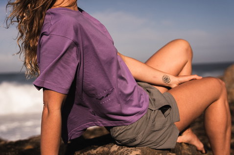 ION Tally boardshorts 2,5" donna in grigio oliva durante una pausa sulle rocce costiere