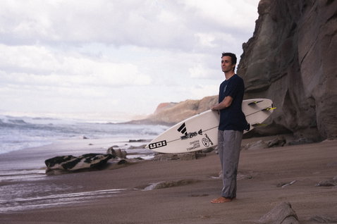 ION Addicted SS men's T-shirt in midnight navy during surfing at a rocky coastal beach