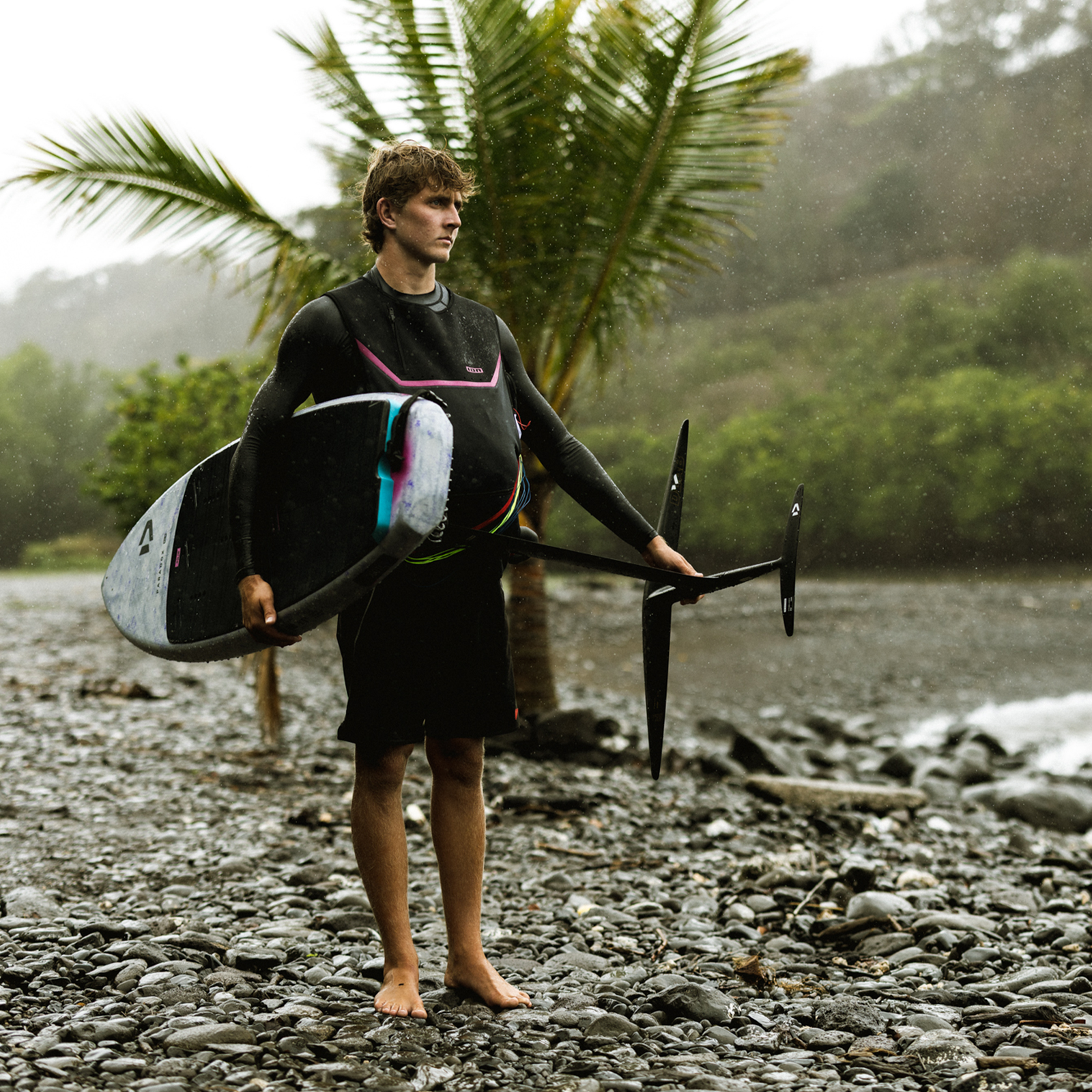 ION Jam neo water jacket unisex in dark olive during wing foiling on a rocky tropical beach