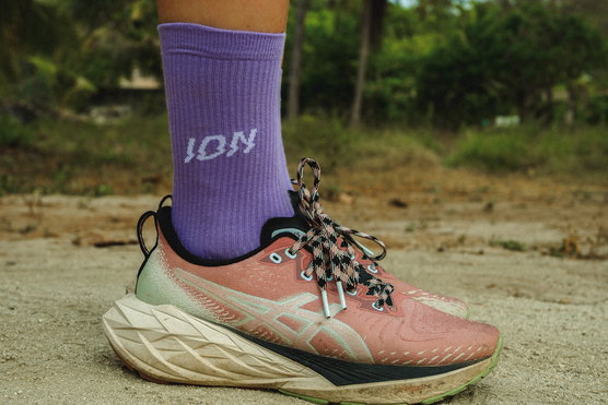 ION Ionic Light socks in lavender worn on a sandy path in a tropical outdoor setting