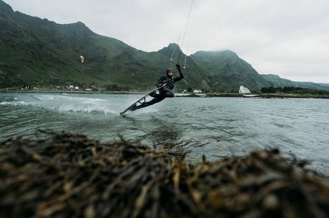 ION Seek Amp 6/5mm front-zip hooded fullsuit in black during kitesurfing on a fjord