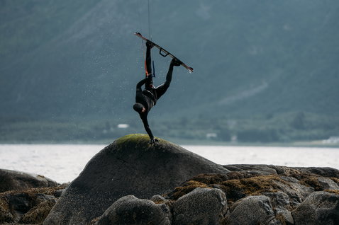 ION Seek Amp 6/5mm hooded front-zip fullsuit in black during kitesurfing at a fjord