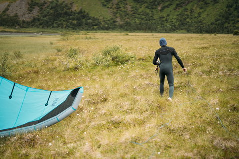 ION Seek Amp 3/2mm front-zip fullsuit during kitesurfing in a highland landscape in olive green