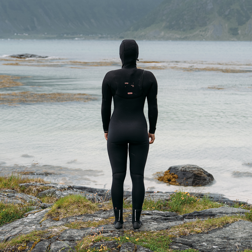 ION Amaze Amp 6/5mm hooded front-zip women's fullsuit in black worn at a rocky coastline