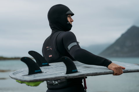 ION Amaze Amp 6/5mm front-zip hooded fullsuit women in black during wave riding at an arctic fjord