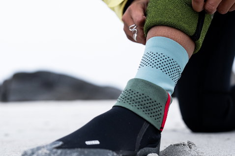 ION Feelgood Socks 4/3 neoprene socks in black, blue and green being put on at the beach
