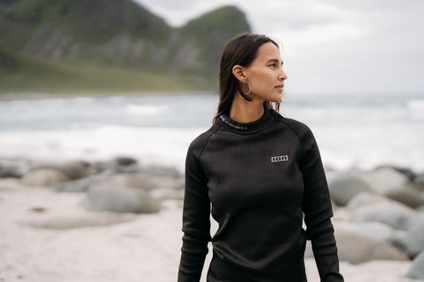 ION Surf Shield long-sleeve rashguard in black during kitesurfing at a rocky coastal beach