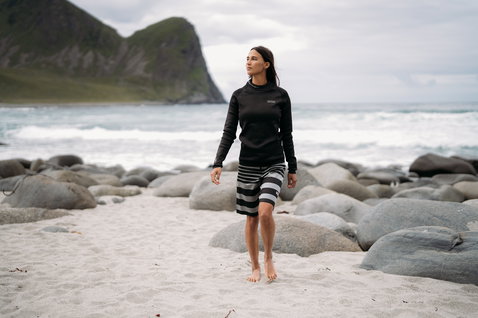 ION Surf Shield long-sleeve rashguard unisex in black during standing pose at rocky ocean beach