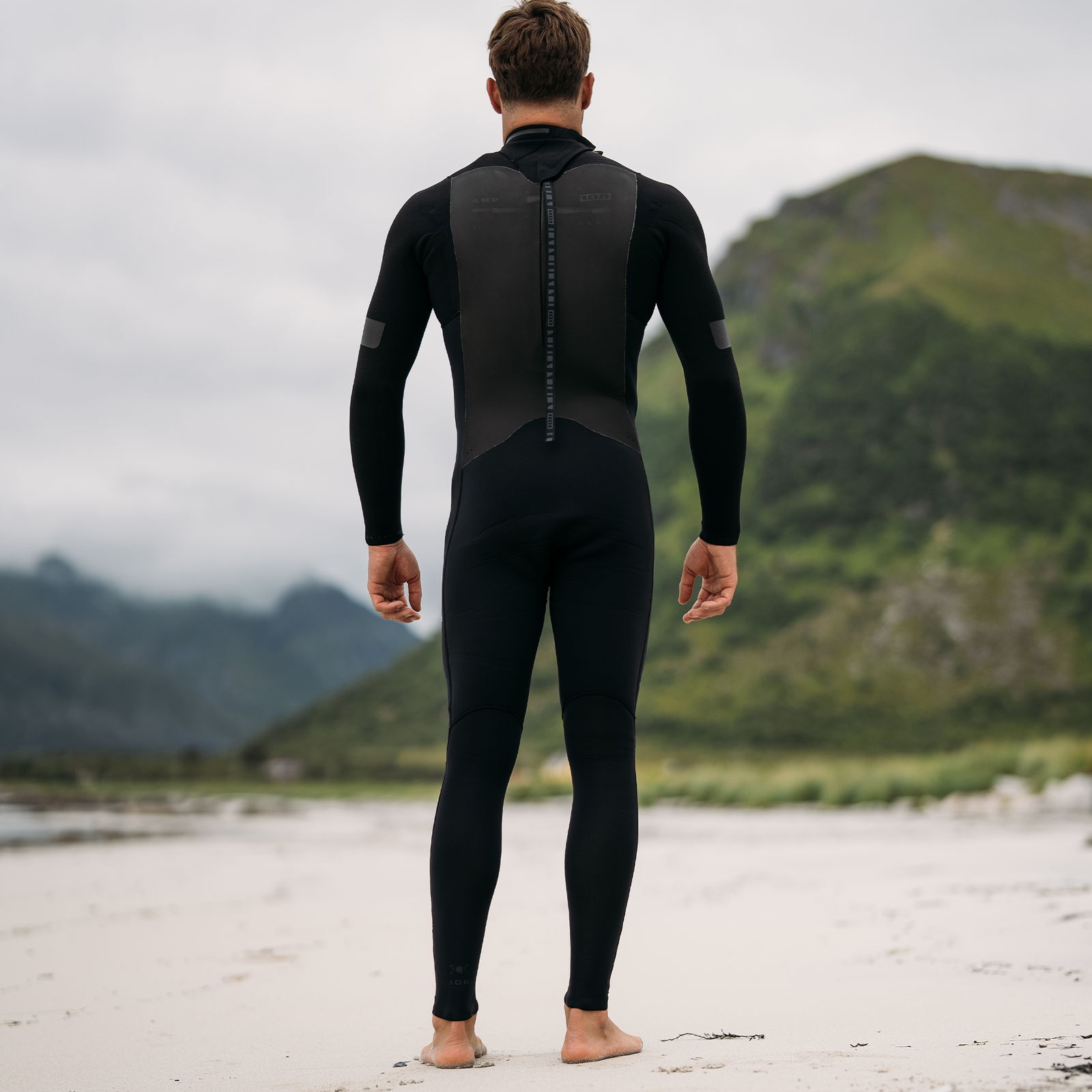 ION Seek Amp 4/3mm back-zip men's fullsuit wetsuit in black, back view on beach