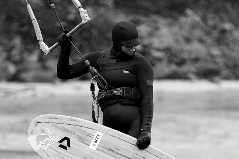 ION Amaze Amp 6/5mm hooded front-zip fullsuit women in black during kitesurfing in the rain