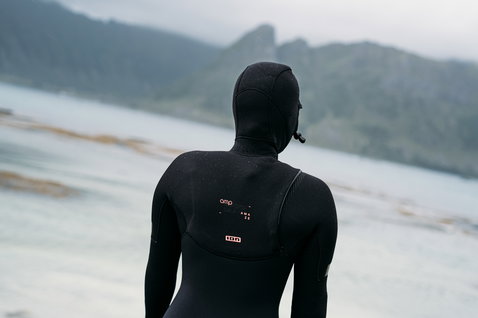 ION Amaze Amp 6/5mm front-zip hooded fullsuit women in black during wave riding at a cold-water coastline