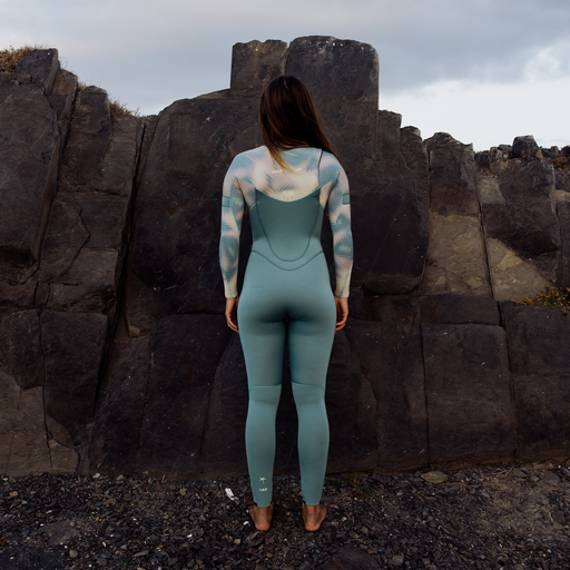 ION Amaze Core 3/2mm Frontzip Neoprenanzug in lagoon green auf Felsküste — Rückansicht