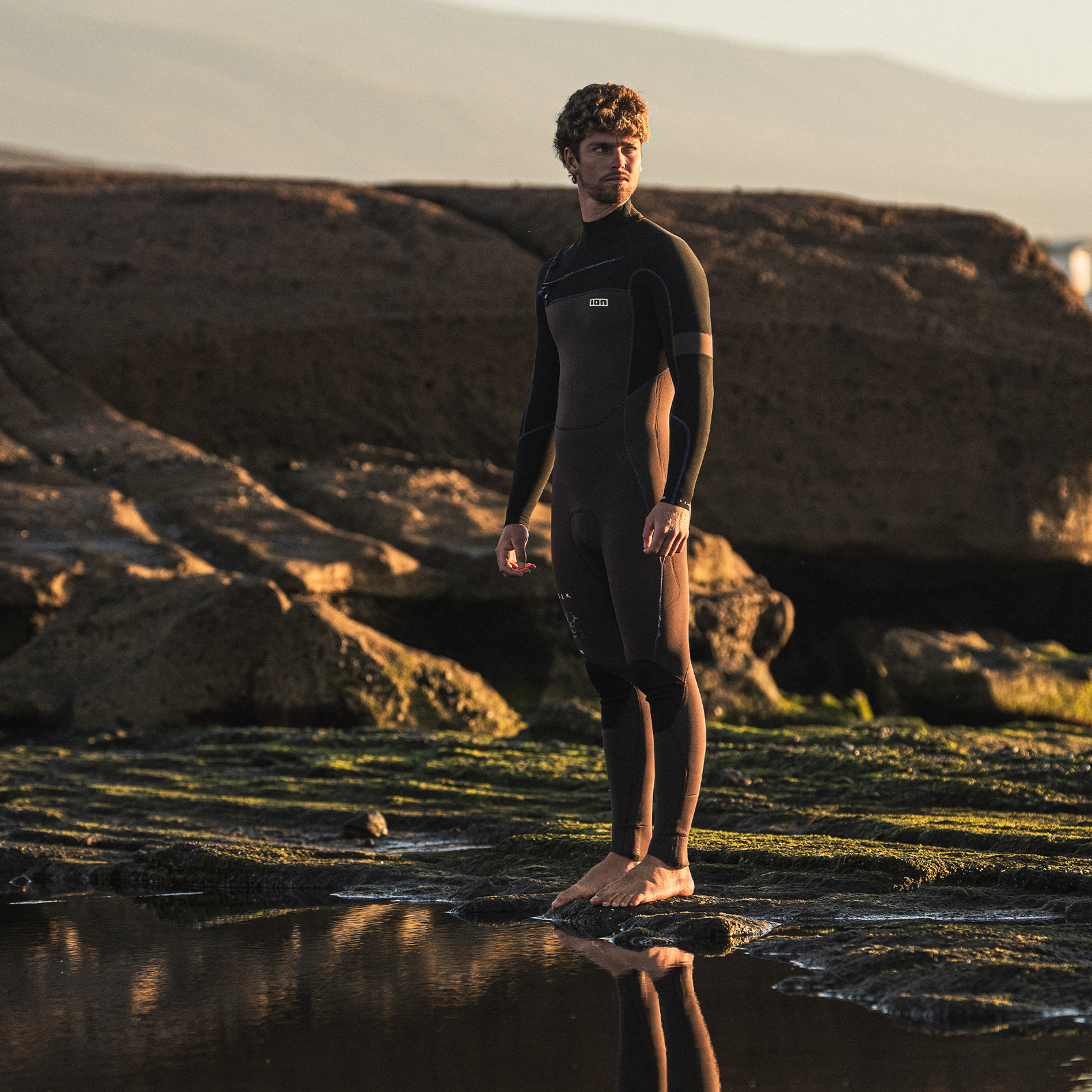 ION Seek Core 4/3mm front-zip fullsuit in seal brown worn at a rocky coast during golden hour