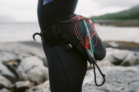 ION Jam waist harness in black during wing foiling at a rocky coastline with parawing lines stored