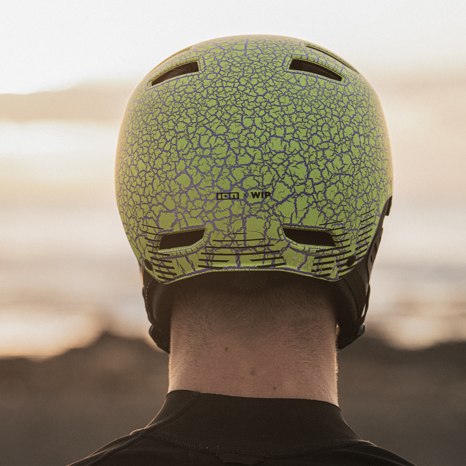 ION Slash Amp helmet in marble lime with crackle pattern seen from behind on a rider at the coast