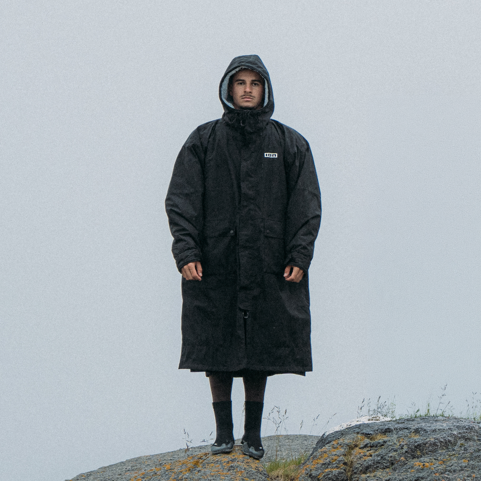 ION Storm Coat changing robe in black worn by a model on a rocky coastal outcrop