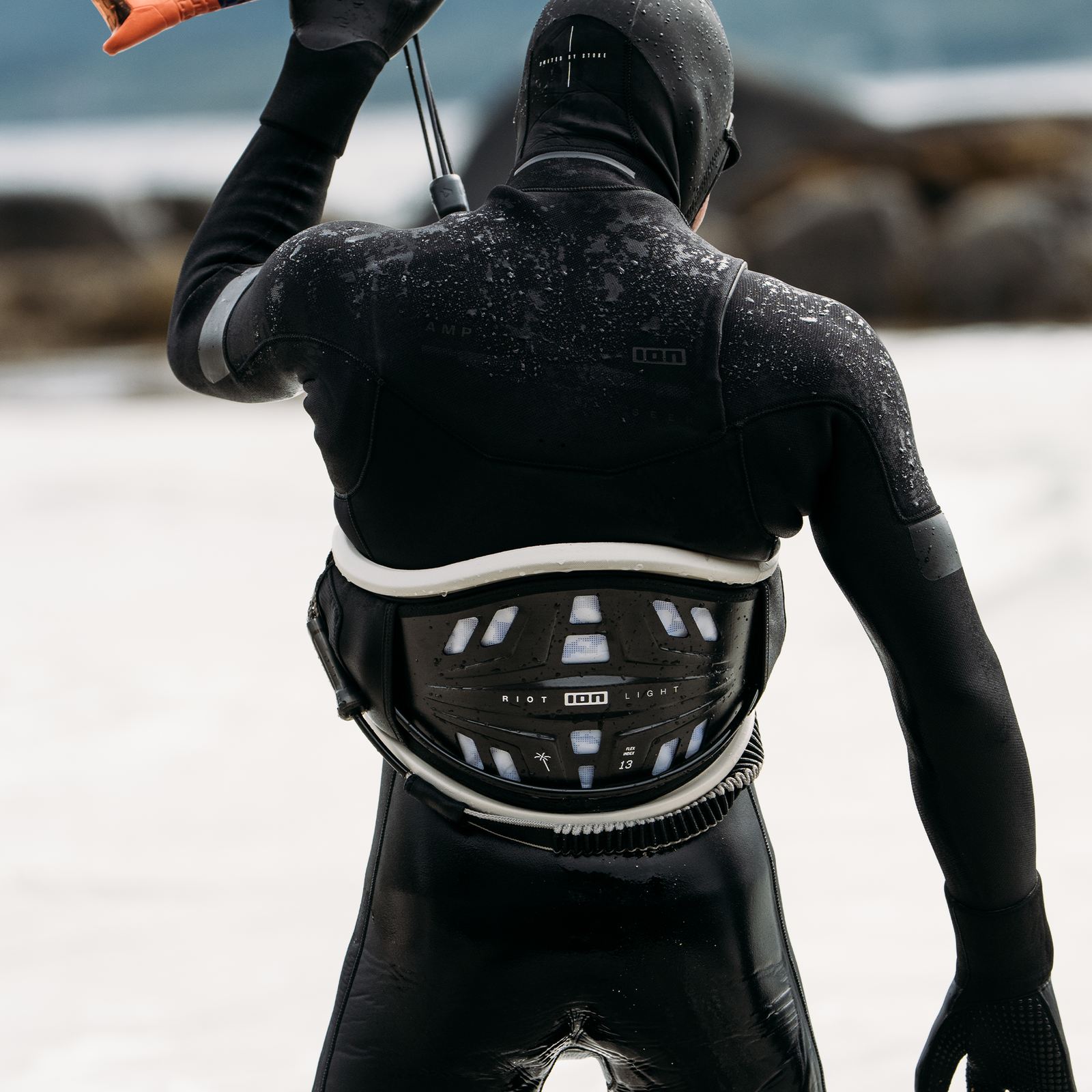 ION Riot Light waist harness in black and white during kitesurfing at a rocky coastline