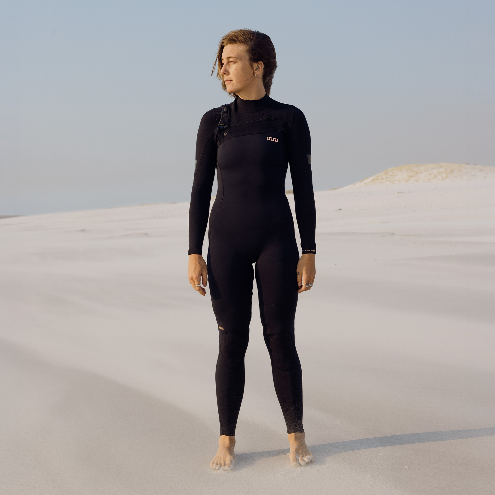 ION Amaze Amp 3/2mm front-zip fullsuit wetsuit for women in black on sandy beach