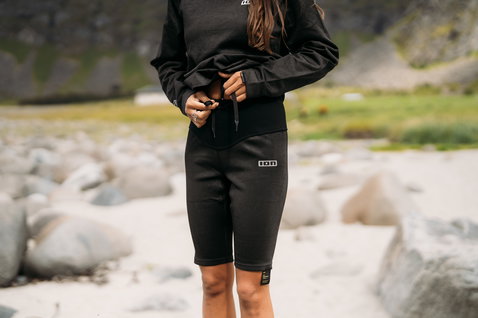 ION Surf Shield bottom tights short in black worn standing at a rocky beach