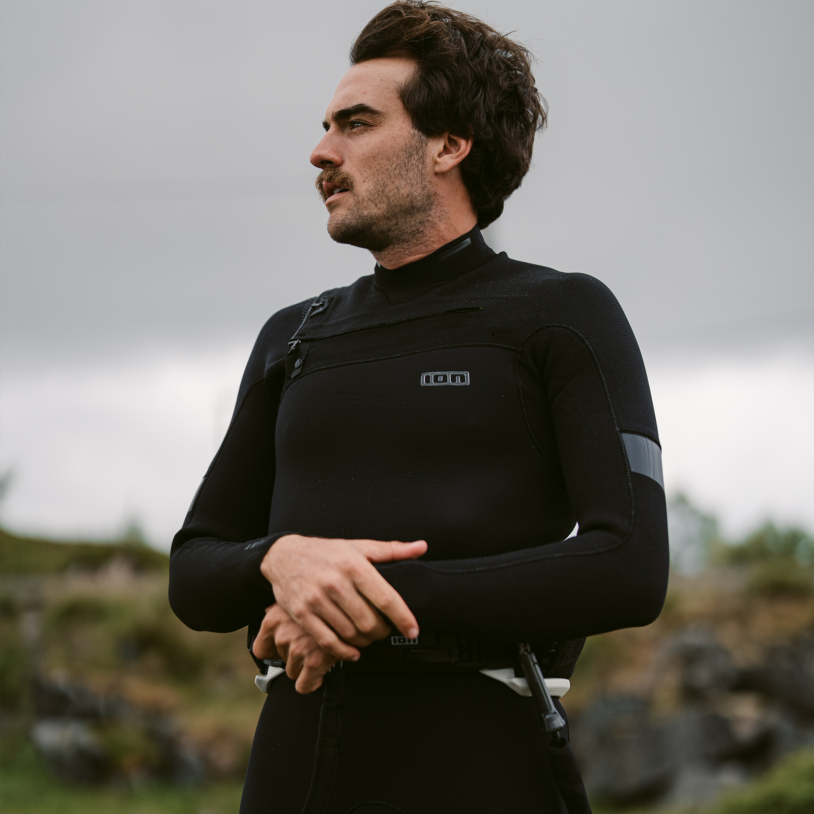 ION Seek Amp 4/3mm front-zip fullsuit for men in black worn at a rocky coastal location